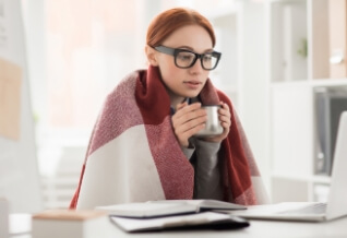 A woman sitting under a blank with a hot drink.