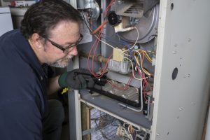 Technician looking over a gas furnace with a flashlight before cleaning it.