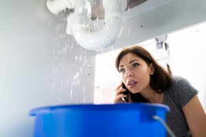 homeowner-looking-under-sink-at-leak-with-phone-to-ear